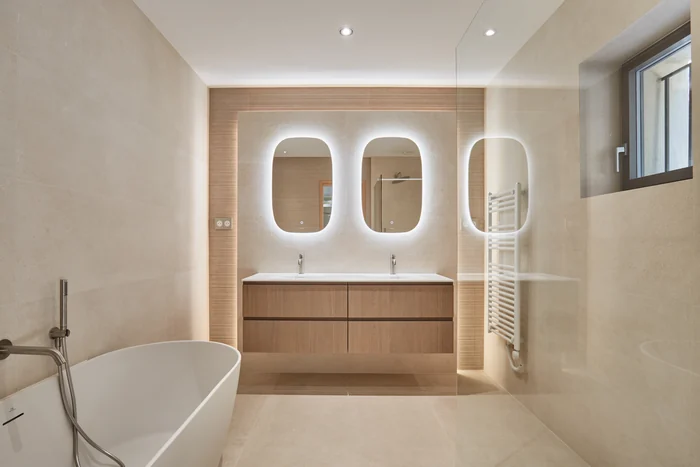 La salle de bain : baignoire îlot, double vasque suspendue et miroirs rétroéclairés